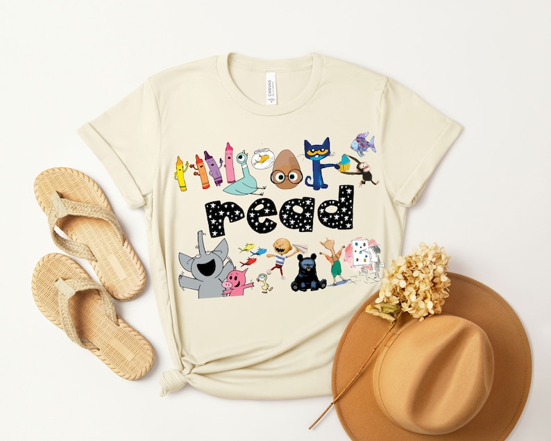 May include: A beige t-shirt with a colorful graphic of characters from the book "The Book With No Pictures". The graphic includes the words "I love to read" and features a variety of characters, including a blue cat, a brown egg, and a pink pig.