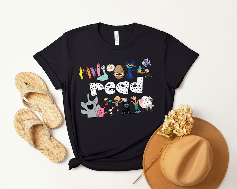 May include: Black t-shirt with a graphic of colorful crayons, a cat, an egg, and other characters. The text "Read" is in white with black polka dots.