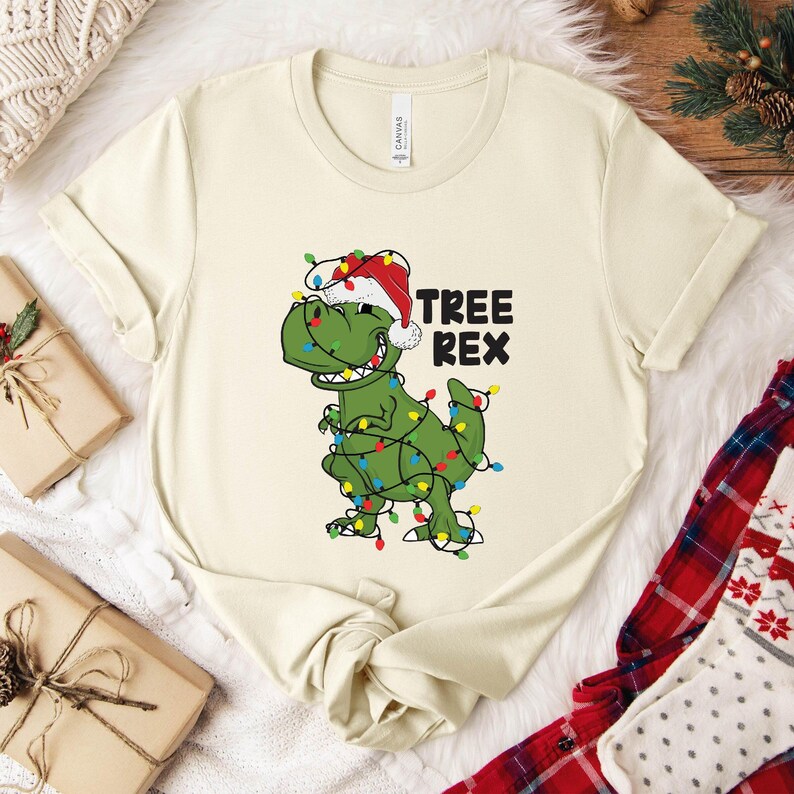 a white t - shirt with a green dinosaur wearing a santa hat