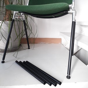 May include: A modern chair with a green fabric seat and backrest, supported by a silver metal frame and black legs. The chair is shown with extra black metal legs. The chair is designed for comfort and style.