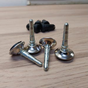 May include: A collection of metal furniture feet with a silver finish and a black rubber base. The feet have a round base and a threaded post. Several black plastic clips are in the background.