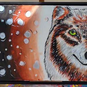 May include: A framed canvas painting depicting a wolf's face on the right, set against a gradient background of black, brown, and white. The wolf has orange, white, and grey fur, with a striking green eye. Silver and white circular accents are scattered across the background.