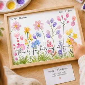 Puede incluir: Una impresión floral enmarcada con el texto «Gracias por ayudarnos a crecer». La obra de arte presenta flores coloridas y el texto «Clase de 2024» y «Para la Sra. Chapman». Una tarjeta dice «Hazlo personal, cada niño añade su huella dactilar».