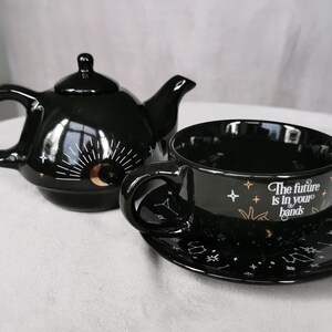 May include: Black tea set featuring a teapot and a cup and saucer. The teapot and cup have a celestial design with stars, moons, and the text "The future is in your hands".