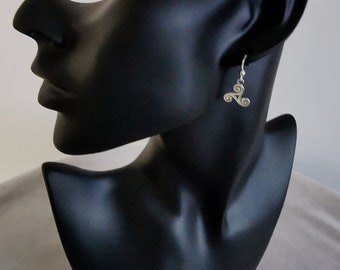 May include: Silver earrings with a triple spiral design. The earrings are hanging from a black mannequin's ear.