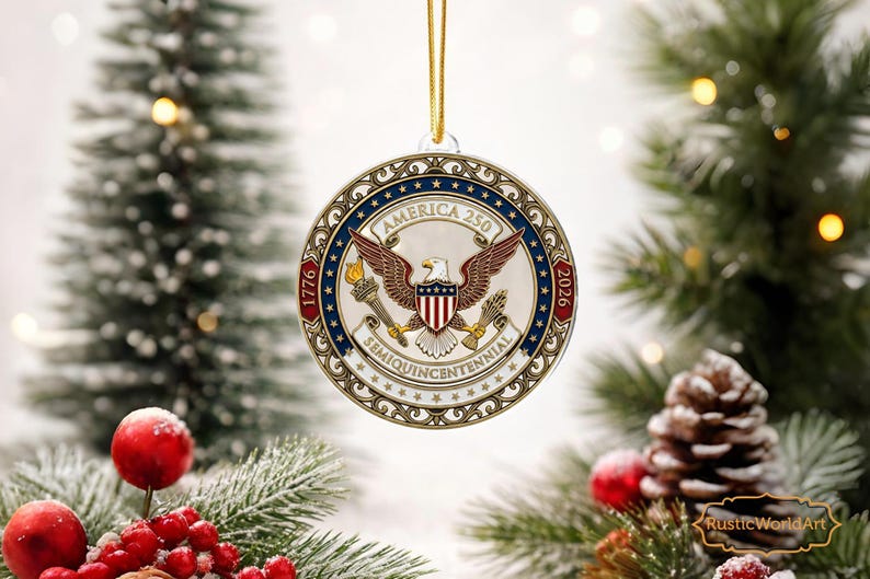 May include: A round Christmas ornament with a patriotic design. The ornament features an eagle, the text "America 250", and the years "1776" and "2026". It is suspended by a gold string and set against a festive background.