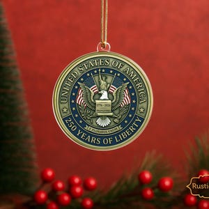 May include: A gold-colored round Christmas ornament with the text "UNITED STATES OF AMERICA" and "250 YEARS OF LIBERTY". The ornament features an eagle, American flags, and the Statue of Liberty. The background is red.