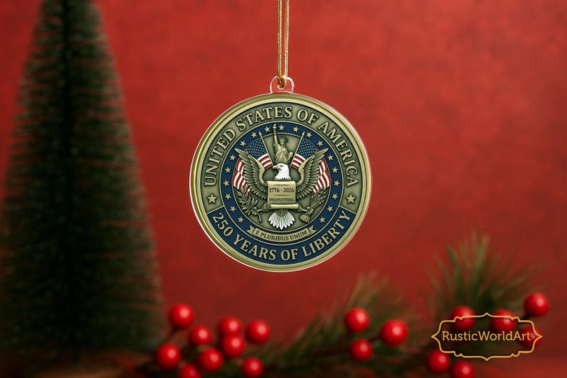May include: A gold-colored round Christmas ornament with the text "UNITED STATES OF AMERICA" and "250 YEARS OF LIBERTY". The ornament features an eagle, American flags, and the Statue of Liberty. The background is red.