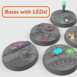 Puede incluir: Cinco bases redondas de plástico gris con diferentes diseños que incluyen luces LED. Las luces son rojas, verdes, azules, amarillas y moradas. Las bases son para figuras en miniatura y están etiquetadas como "¡Bases con LED!"