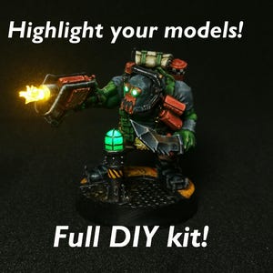 Puede incluir: Una figura en miniatura verde y negra de un Ork sosteniendo un arma con una punta amarilla brillante. La figura está de pie sobre una base negra con una luz verde brillante. El texto "¡Resalta tus modelos!" y "¡Kit completo de bricolaje!" es visible en la imagen.