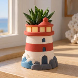 May include: A lighthouse-shaped planter featuring a red and white striped tower, a blue arched door, and blue wave accents at the base. The planter holds a green succulent plant with pointed leaves, and the top section has a yellow glow.