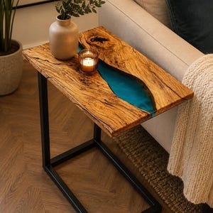Puede incluir: Una mesa auxiliar rectangular con un tablero de madera natural de borde irregular y una incrustación central de resina azul vibrante. La mesa está sostenida por una estructura de metal negro con una base en forma de C para muebles.