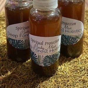 May include: Three brown glass bottles with spray tops and labels. The labels have a green leafy design and text that reads "Spiritual Protection Body Mist Deep Forest Holistics".