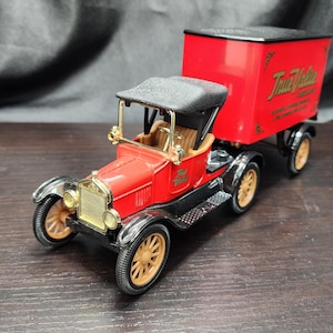 May include: A red and black vintage toy truck with a trailer. The truck has gold-colored wheels and trim, and a black roof. The trailer is red with gold lettering. The truck is a replica of a classic vehicle.