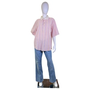 May include: A mannequin wearing a red and white striped polo shirt with a white collar and blue jeans. The shirt has short sleeves and a button-up neckline. The jeans are flared at the bottom.