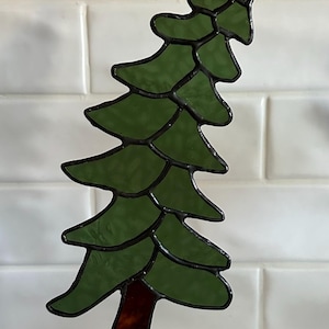 Peut inclure: Un arbre en vitrail avec un tronc brun foncé et des feuilles vertes. L'arbre est posé sur une base en bois.