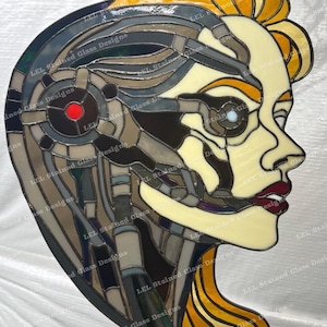 May include: Stained glass artwork depicting a profile of a cyborg woman. The piece features a palette of beige, gray, brown, and yellow, with red lips and a red eye. The text "LEL Stained Glass Designs" is visible.