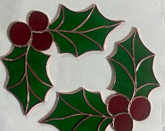 Op de afbeelding: Drie glas-in-lood kerstversieringen in de vorm van hulstbladeren met rode bessen. De bladeren zijn groen met koperfolie omranding.