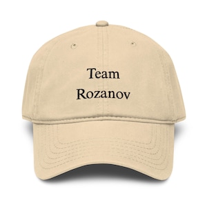 Könnte beinhalten: Beige Baseball Cap mit dem schwarzen Text "Team Rozanov" auf der Vorderseite. Die Kappe hat einen gebogenen Schirm und einen Knopf oben.