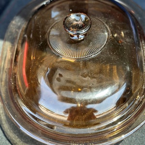 May include: A brown glass casserole dish with a lid. The lid has a knob on top and the dish has the word "Corning" and "USA" printed on the bottom.