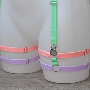 May include: Three adjustable garter belts in pastel colours: light green, pink, and lavender. The garter belts are made of elastic fabric and have metal clasps.