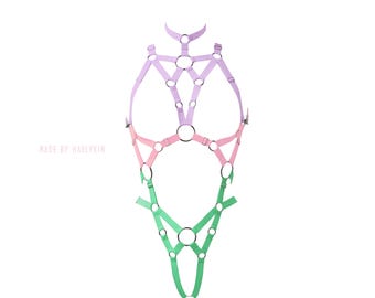 May include: A pastel pink, green, and purple body harness with multiple straps and rings. "MADE BY HARLYKIN" is written in the lower left corner.