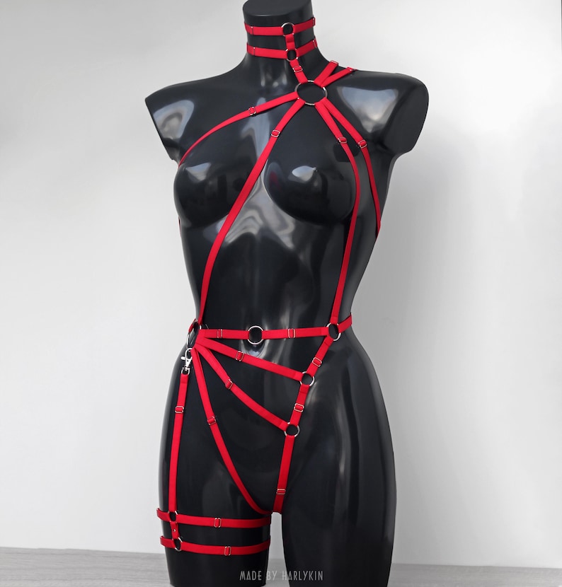 May include: Red body harness with silver rings and straps. The harness has a choker style neckline and thigh straps. "MADE BY MARLYKIN" is printed on the bottom of the image.