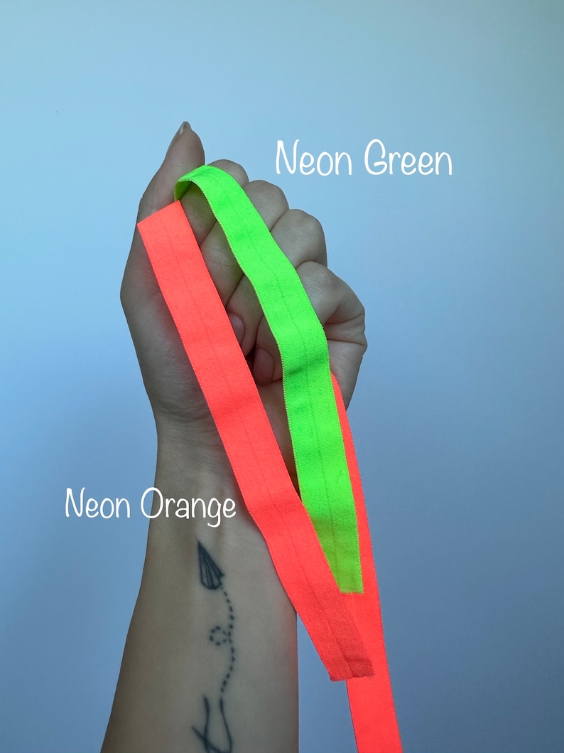 May include: Two neon colored elastic bands, one neon green and one neon orange, are held in a hand. The text "Neon Green" is above the green band and the text "Neon Orange" is below the orange band.