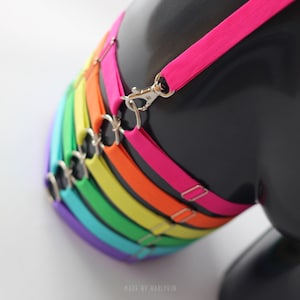 Könnte beinhalten: Ein regenbogenfarbener Satz elastischer Bänder mit silbernen Verschlüssen. Die Bänder sind in der Reihenfolge Lila, Blau, Türkis, Grün, Gelb, Orange und Pink übereinander gelegt.