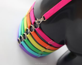 May include: A rainbow-colored set of elastic straps with silver clasps. The straps are layered in the order of purple, blue, turquoise, green, yellow, orange, and pink.