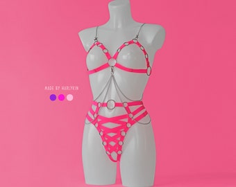 May include: A pink lingerie set with silver hardware and straps. The set includes a bra and a matching panty with a criss-cross design. The set is made by Harlykin.