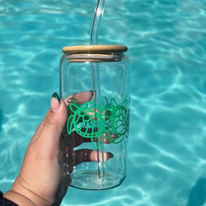 May include: A clear glass water bottle with a wooden lid and a green sea turtle design. The bottle has a clear glass straw.