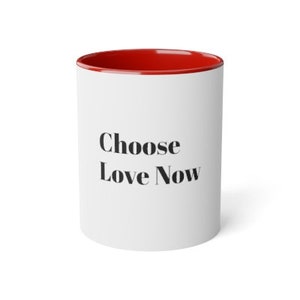 以下が含まれることがあります： 赤い縁取りのある白いセラミック製のコーヒーカップ。カップには黒い文字で「Choose Love Now」と印刷されています。