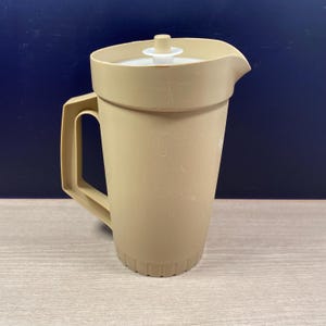 May include: A tan plastic pitcher with a matching lid and handle. The pitcher has a spout for pouring and a ridged base. The lid is white and has a small handle. The pitcher is designed for serving beverages.