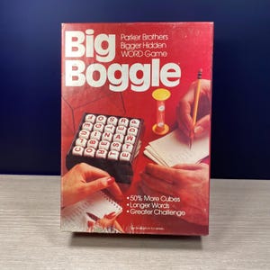 May include: A vintage Big Boggle word game box with a red background. The box features the game's name, a cube tray with lettered dice, an hourglass, and text that reads "50% More Cubes, Longer Words, Greater Challenge."