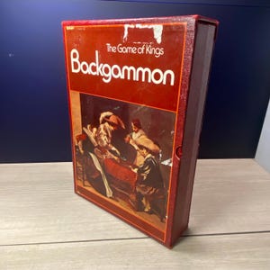 May include: A vintage Backgammon game box in shades of red and brown. The box features the text "The Game of Kings" and "Backgammon" in white. The box art depicts a historical scene of people playing the game. The box is rectangular and has a red border.