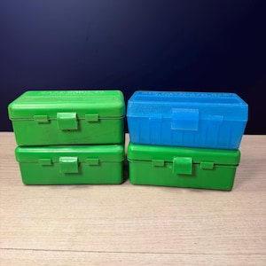 May include: Four rectangular plastic storage cases with hinged lids and latch closures. Two cases are solid green, one is solid green with a textured top, and one is translucent blue. The green cases feature embossed text on the lids.