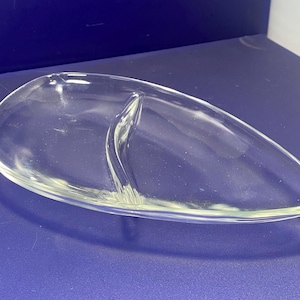 May include: Clear glass serving dish with two compartments. The dish has a teardrop shape with a divider down the middle. The glass is smooth and transparent, allowing a clear view of the contents.