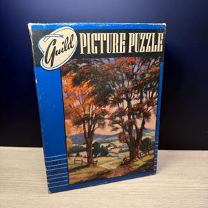May include: A vintage Guild Picture Puzzle box with a landscape scene. The box is blue with the words "PICTURE PUZZLE" in white. The puzzle image depicts trees with orange and brown leaves, a path, and a fence.