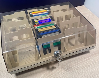 May include: A vintage beige and clear plastic floppy disk storage case with a lock and key. The case is filled with colorful 3.5-inch floppy disks and dividers. Some handwritten notes are visible inside the case.