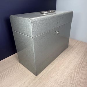 May include: A silver metal storage box with a textured surface. The box has a handle on top and a latch on the front. The box is rectangular and appears to be made of metal.