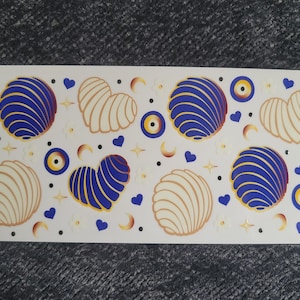 Op de afbeelding: Een vel wit stickerpapier met blauwe en witte schelpvormige stickers, blauwe en gouden hartvormige stickers en blauwe en gouden boze oog stickers.