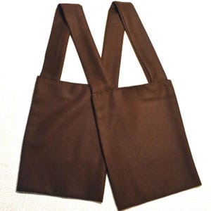 May include: A pair of brown fabric straps, likely for a bag or apron, are displayed against a white background. The straps are rectangular at the bottom and taper to form a V-shape at the top, suggesting they are designed to be worn over the shoulders.