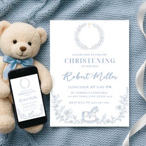 Könnte beinhalten: Eine weiße Einladung mit blauem Text und floralen Akzenten kündigt eine Taufe an. Der Text lautet: "Bitte begleiten Sie uns zur Taufe unseres Sohnes Robert Miller." Ein Smartphone zeigt die gleiche Einladung an. Ein Teddybär mit einer blauen Schleife ist im Hintergrund.