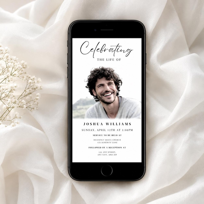 May include: A mobile phone screen shows a memorial invitation. The text reads "Celebrating the Life of Joshua Williams." The invitation includes the date, time, and location of the service and reception. The background is a soft white fabric.