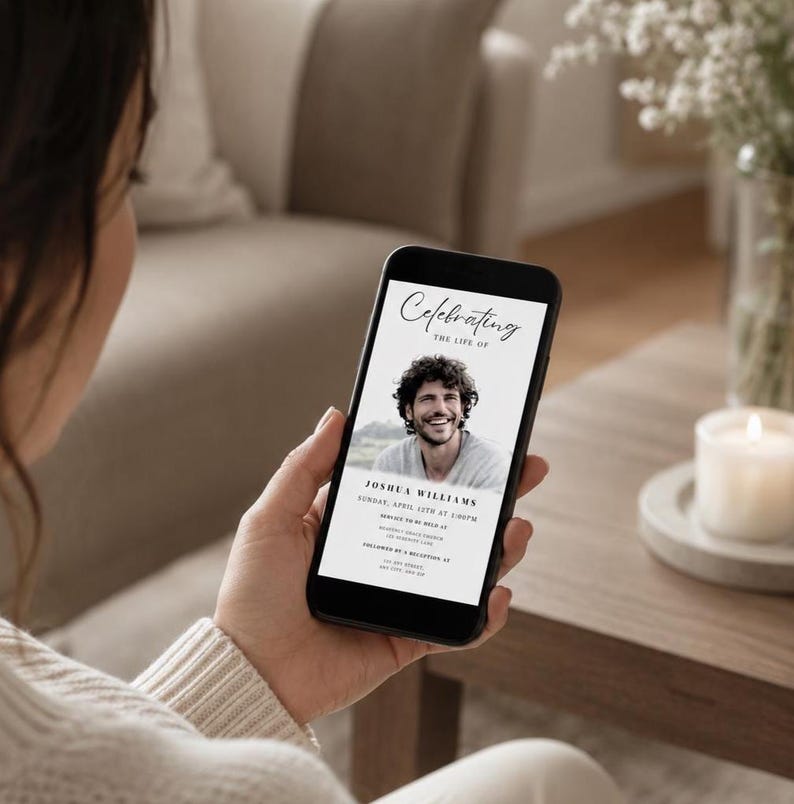 May include: A person holding a smartphone showing a memorial invitation. The invitation has a photo of a smiling man, the text "Celebrating the Life of Joshua Williams," and event details in black on a white background.