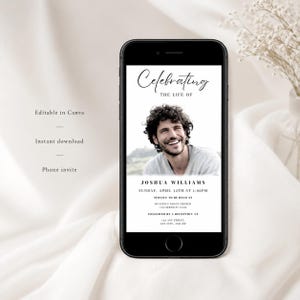 May include: A black smartphone shows a memorial invitation. The invitation includes a photo of a smiling man, with the text "Celebrating the Life of Joshua Williams." The date, time, and location of the service are also displayed. The phone rests on a white surface.