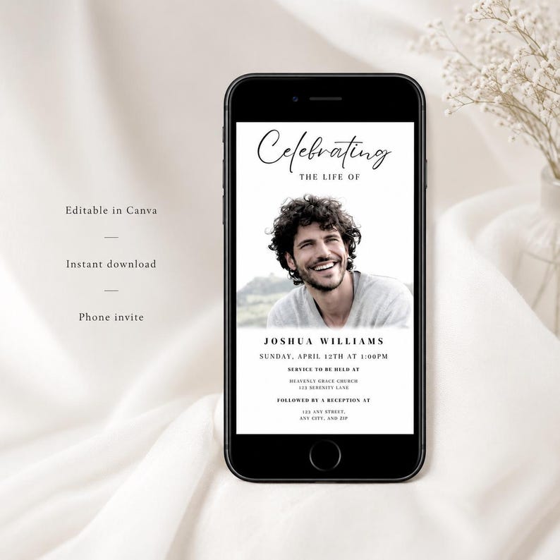 May include: A black smartphone shows a memorial invitation. The invitation includes a photo of a smiling man, with the text "Celebrating the Life of Joshua Williams." The date, time, and location of the service are also displayed. The phone rests on a white surface.