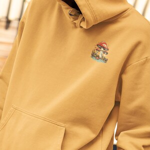 May include: A mustard yellow hoodie with a mushroom graphic on the front. The hoodie has a drawstring hood and a kangaroo pocket.