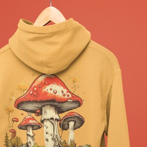 May include: A mustard yellow hoodie with a graphic of three red and white mushrooms in a forest setting. The mushrooms are surrounded by green foliage and a blue stream.